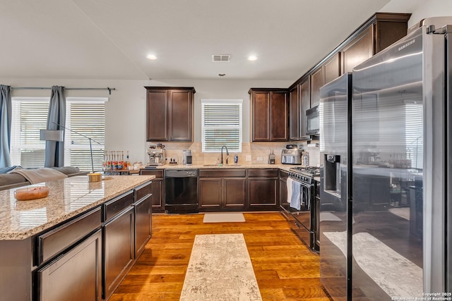 kitchen featuring light stone countertops, light wood-type flooring, tasteful backsplash, sink, and black appliances