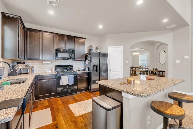 kitchen featuring light stone countertops, sink, tasteful backsplash, a kitchen island, and black appliances