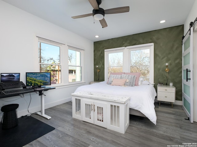 bedroom with dark wood-type flooring, ceiling fan, and a barn door