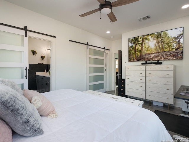 bedroom with ensuite bathroom, ceiling fan, a barn door, and dark wood-type flooring