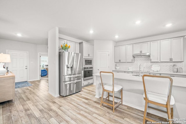 kitchen featuring light wood-type flooring, backsplash, stainless steel appliances, sink, and a breakfast bar area