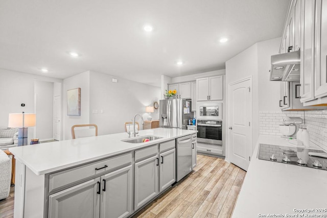 kitchen with sink, stainless steel appliances, range hood, a center island with sink, and light wood-type flooring