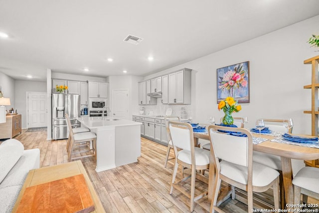 kitchen featuring built in microwave, sink, tasteful backsplash, stainless steel refrigerator with ice dispenser, and a kitchen island with sink