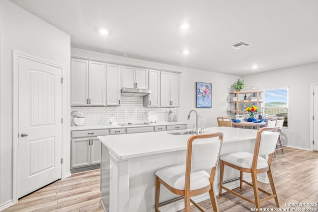 kitchen with sink, a kitchen bar, an island with sink, and light wood-type flooring