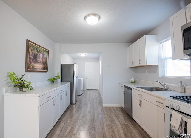 kitchen with sink, appliances with stainless steel finishes, a textured ceiling, white cabinets, and light wood-type flooring