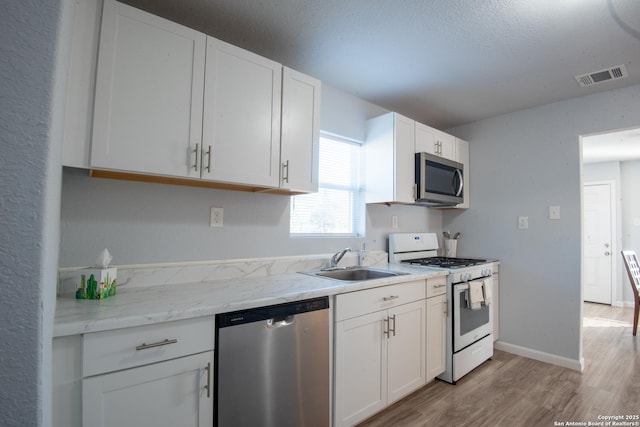 kitchen featuring sink, stainless steel appliances, light stone counters, light hardwood / wood-style floors, and white cabinets