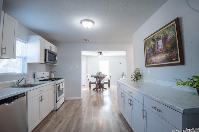 kitchen featuring appliances with stainless steel finishes, light wood-type flooring, a textured ceiling, sink, and white cabinetry