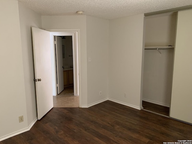 unfurnished bedroom with a textured ceiling, dark hardwood / wood-style floors, and a closet