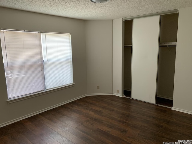 unfurnished bedroom with dark hardwood / wood-style flooring, a textured ceiling, and multiple windows