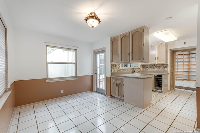 kitchen with kitchen peninsula, backsplash, beverage cooler, sink, and light tile patterned flooring