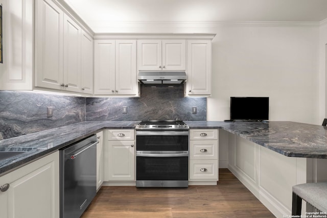 kitchen with dark wood-type flooring, white cabinets, dark stone countertops, kitchen peninsula, and stainless steel appliances