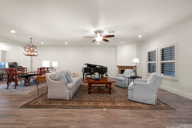 living room with dark wood-type flooring, ceiling fan with notable chandelier, and ornamental molding