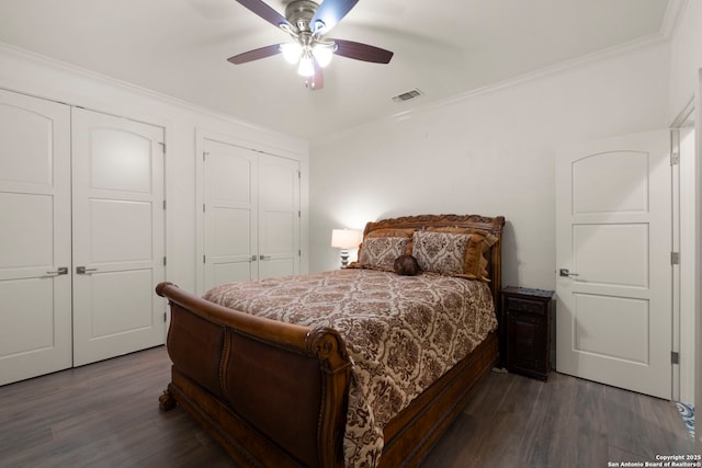 bedroom with two closets, crown molding, ceiling fan, and dark wood-type flooring