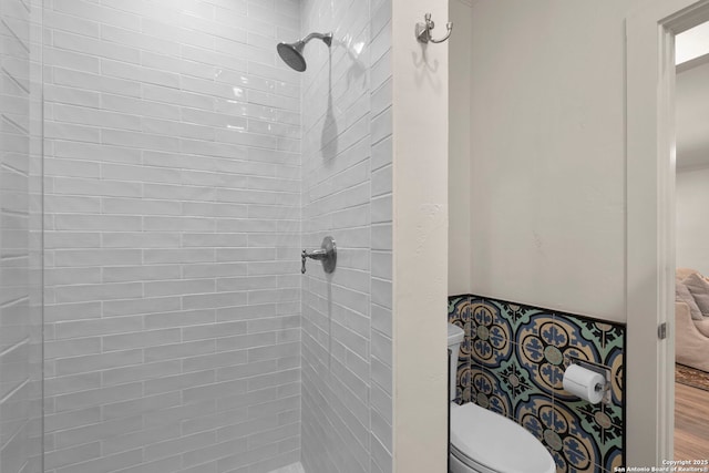 bathroom featuring toilet, a tile shower, and wood-type flooring