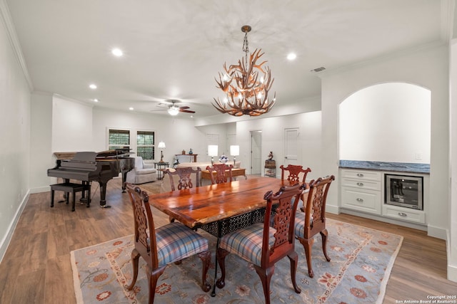 dining space with ceiling fan with notable chandelier, light hardwood / wood-style flooring, beverage cooler, and ornamental molding