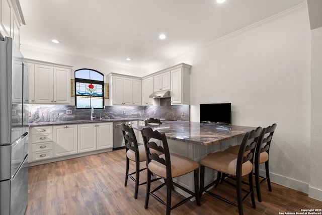 kitchen with dark wood-type flooring, white cabinets, a breakfast bar area, kitchen peninsula, and stainless steel appliances