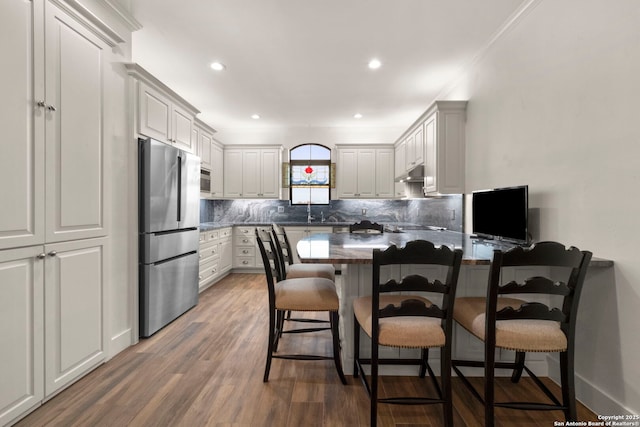 kitchen featuring a kitchen bar, backsplash, dark hardwood / wood-style flooring, stainless steel appliances, and white cabinets