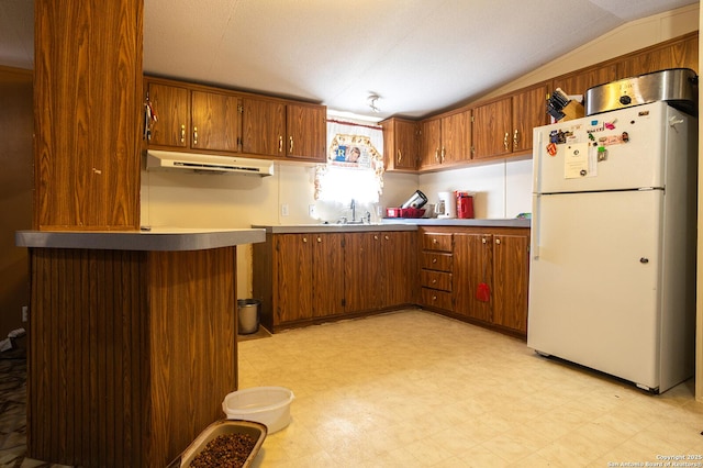 kitchen with white refrigerator, sink, and vaulted ceiling