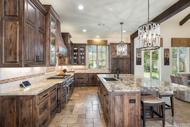 kitchen with glass insert cabinets, decorative light fixtures, a sink, visible vents, and stone tile flooring