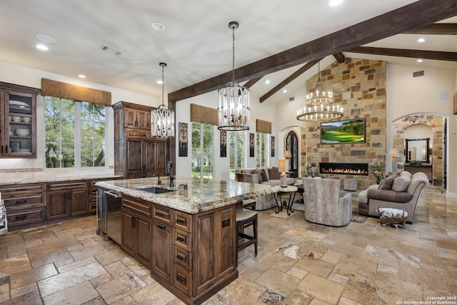 kitchen featuring glass insert cabinets, stone tile floors, a sink, open floor plan, and a center island with sink