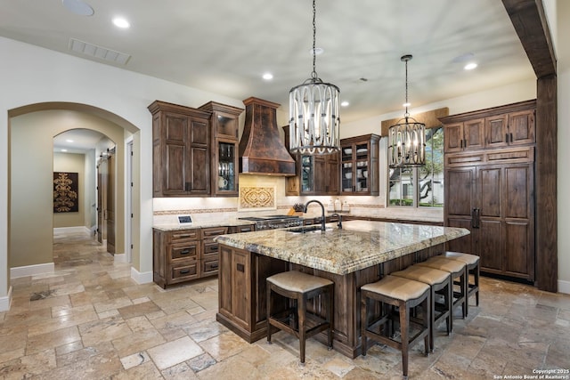 kitchen with an island with sink, light stone countertops, glass insert cabinets, and stone tile floors