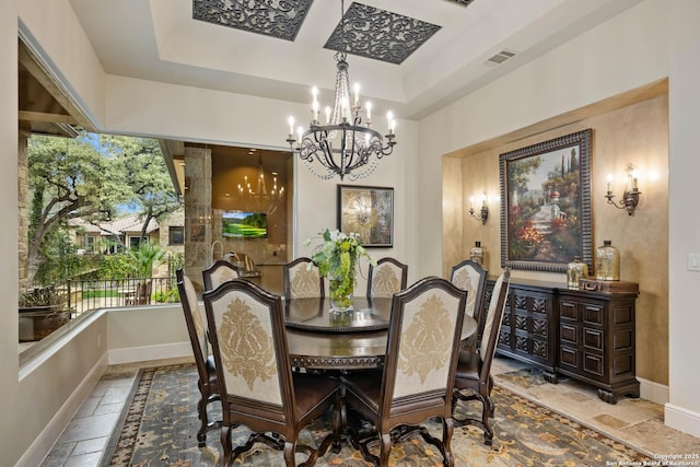 dining room featuring stone tile flooring, a raised ceiling, visible vents, a chandelier, and baseboards