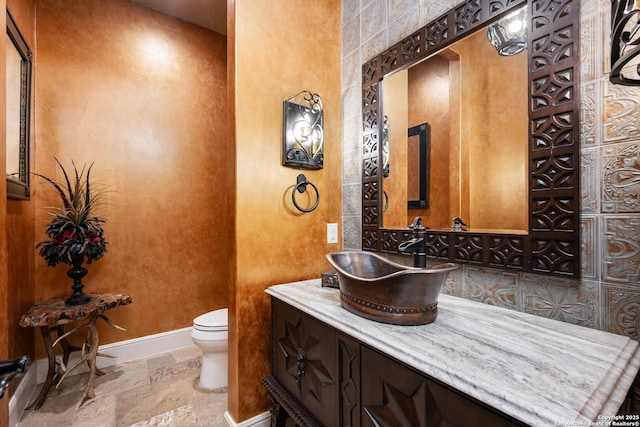 half bathroom featuring baseboards, vanity, toilet, and stone tile floors