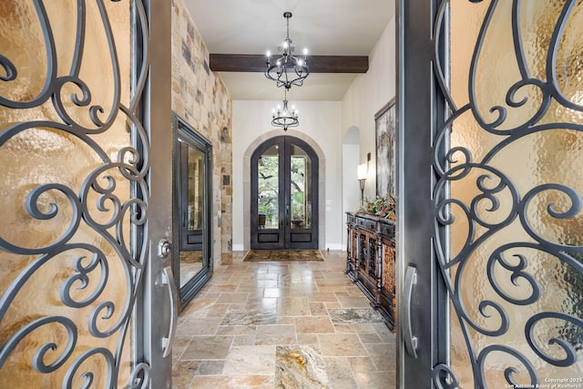 entrance foyer featuring arched walkways, stone tile flooring, french doors, a chandelier, and beam ceiling