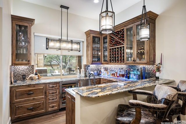 bar with dark wood-style floors, wine cooler, hanging light fixtures, decorative backsplash, and wet bar