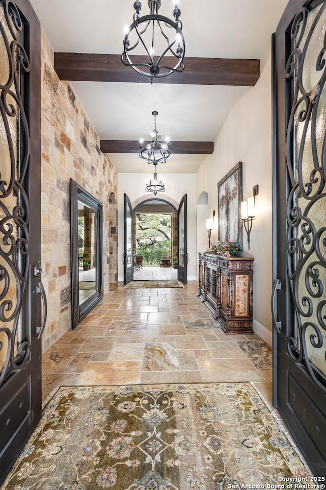 foyer with arched walkways, stone tile floors, baseboards, beamed ceiling, and an inviting chandelier