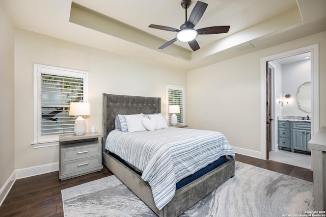 bedroom featuring dark wood-style floors, a raised ceiling, ensuite bath, and baseboards