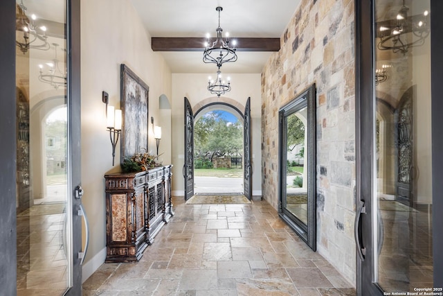 foyer featuring stone tile floors, baseboards, arched walkways, a chandelier, and beam ceiling