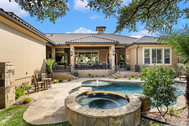 back of property with an in ground hot tub, a patio area, a tiled roof, and stucco siding