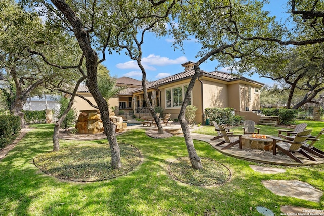 rear view of property with a tile roof, a patio area, a fire pit, and stucco siding