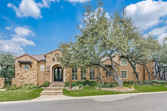 mediterranean / spanish-style home featuring a front yard, stone siding, french doors, and stucco siding