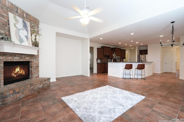 living room with ceiling fan with notable chandelier and a brick fireplace