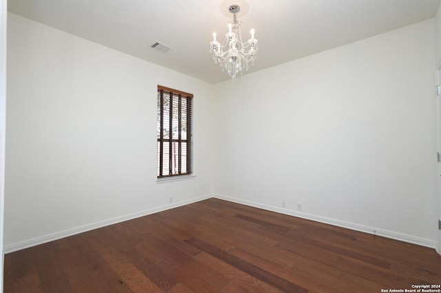 spare room with dark hardwood / wood-style floors and an inviting chandelier