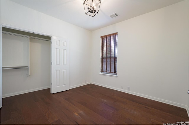 unfurnished bedroom featuring a closet, dark hardwood / wood-style floors, and a notable chandelier