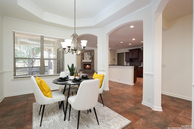 dining area with a raised ceiling, crown molding, a fireplace, and an inviting chandelier