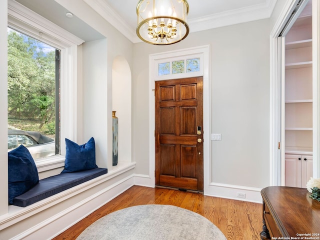 foyer with light hardwood / wood-style floors, crown molding, and a notable chandelier