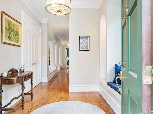 foyer entrance featuring ornate columns, crown molding, light hardwood / wood-style flooring, and an inviting chandelier