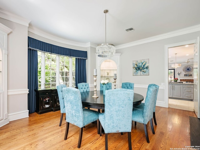 dining space with light wood-type flooring, ornamental molding, and a notable chandelier