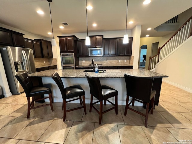 kitchen featuring a kitchen bar, tasteful backsplash, stainless steel appliances, pendant lighting, and dark stone countertops