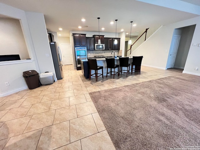 kitchen with appliances with stainless steel finishes, light tile patterned floors, a kitchen island with sink, and a kitchen breakfast bar