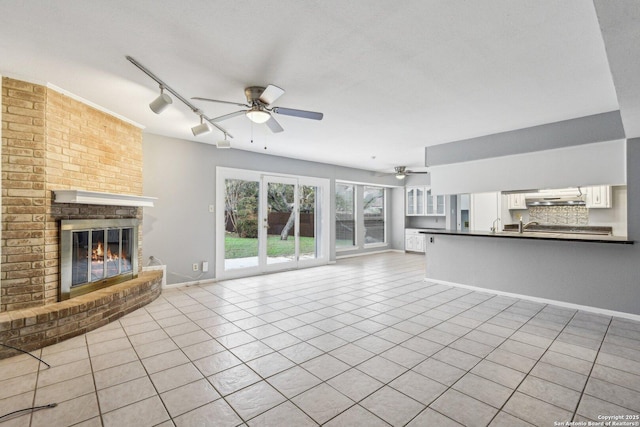 unfurnished living room featuring a fireplace, light tile patterned floors, track lighting, and ceiling fan