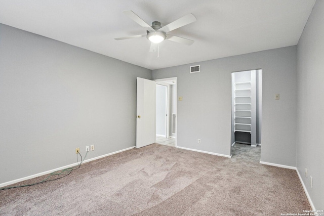 unfurnished bedroom featuring a walk in closet, ceiling fan, a closet, and light carpet