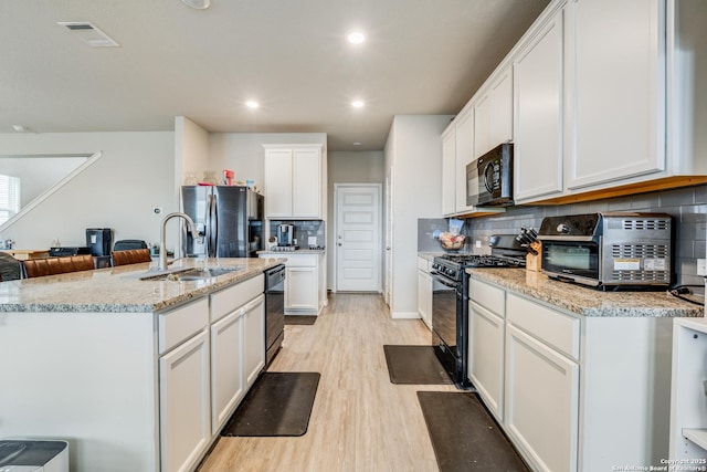 kitchen with black appliances, white cabinets, decorative backsplash, light stone countertops, and light hardwood / wood-style floors