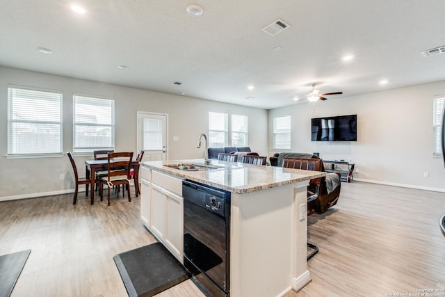 kitchen with light stone countertops, white cabinets, sink, a center island with sink, and dishwasher