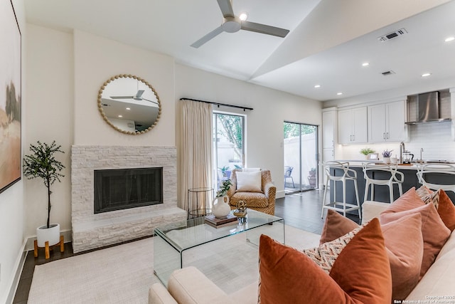 living room with vaulted ceiling, ceiling fan, sink, hardwood / wood-style flooring, and a fireplace