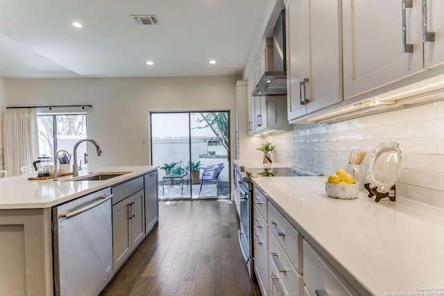 kitchen featuring appliances with stainless steel finishes, a kitchen island with sink, sink, wall chimney range hood, and gray cabinets